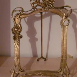Złota, ozdobna rama na zdjęcie w stylu Art Nouveau z metalową podpórką, ustawiona na drewnianej powierzchni.