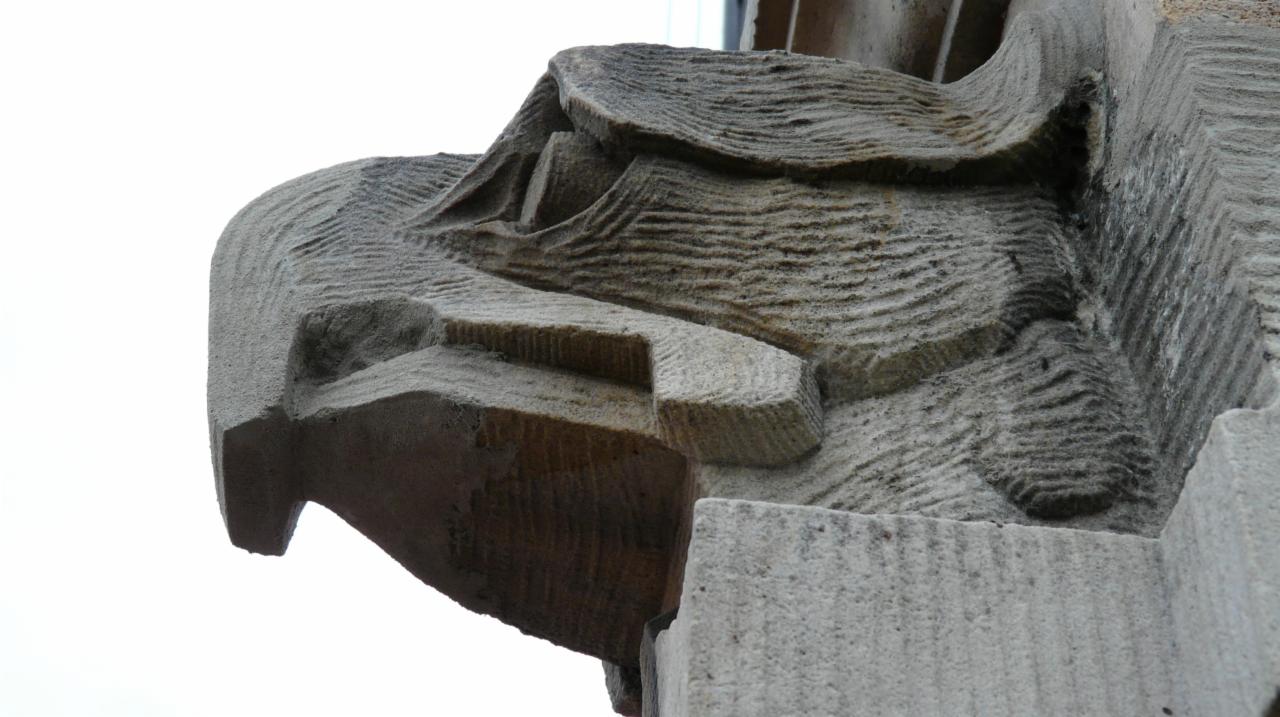 Detal architektoniczny z piaskowca: rzeźbiony element fasady z widocznymi śladami obróbki kamieniarskiej i delikatnymi wzorami erozji.