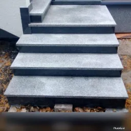 Zewnętrzne schody wejściowe z szarego granitu z czarnymi obrzeżami i stopniami, widok z przodu, liście na dole.