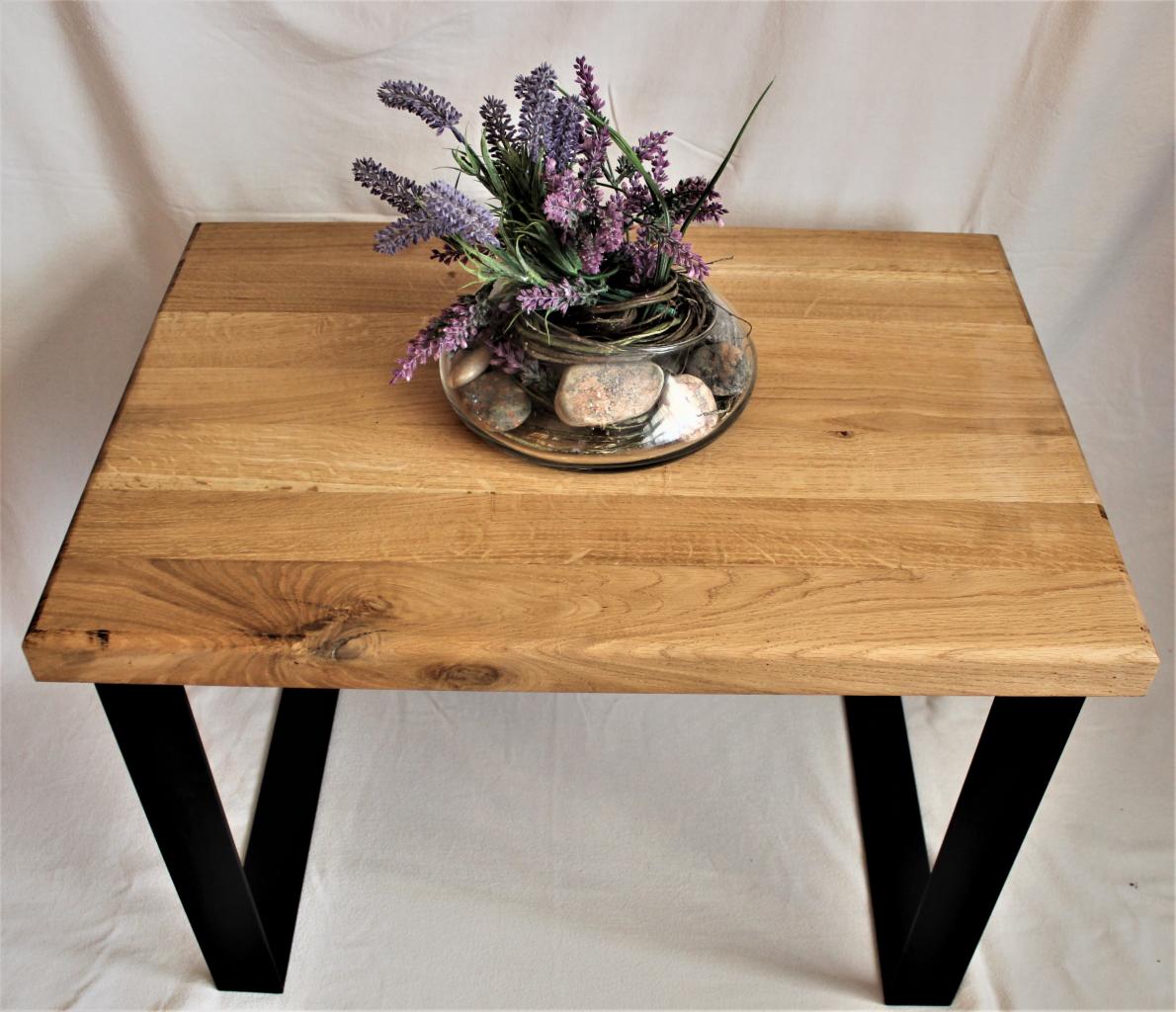 Stolik kawowy z blatem z jasnego drewna dębowego, na czarnych, metalowych nogach w kształcie litery V, udekorowany szklanym wazonem z lawendą i kamieniami.