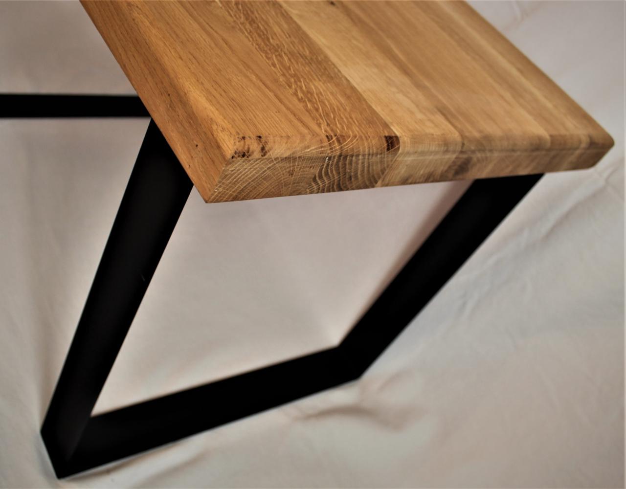Blat drewniany z widocznymi słojami i sękami, wsparty na czarnych, metalowych nogach w kształcie trapezu, na białym tle.