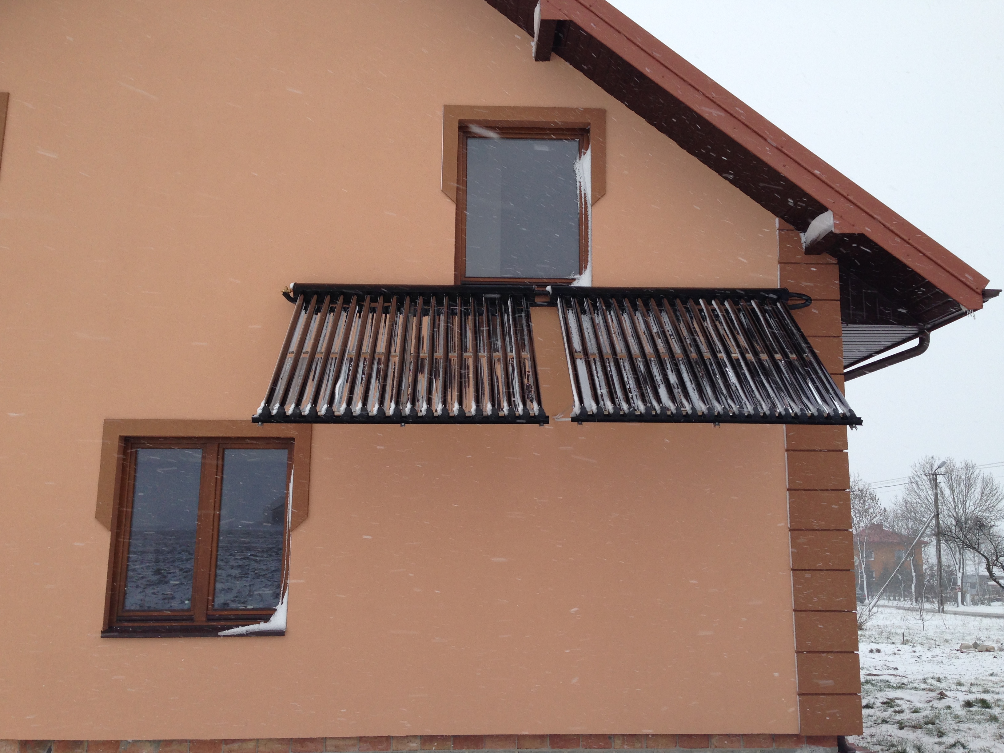 Dwa panele słoneczne kolektorów rurowych zamontowane na elewacji domu w zimowy dzień podczas opadów śniegu.