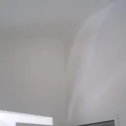 Świeżo pomalowany róg pokoju z idealnie gładkimi ścianami i sufitem, widoczne delikatne ślady po wałku na suficie.