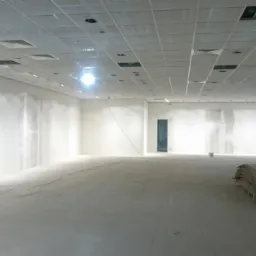 Rozległe wnętrze w trakcie prac wykończeniowych: sufit podwieszany, ściany przygotowane pod malowanie, widoczne kable i drabina. Przygotowanie do instalacji elektrycznej.