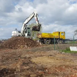 Biała koparka Liebherr nabiera gruz z pryzmy obok żółtej ciężarówki na placu budowy w słoneczny dzień.