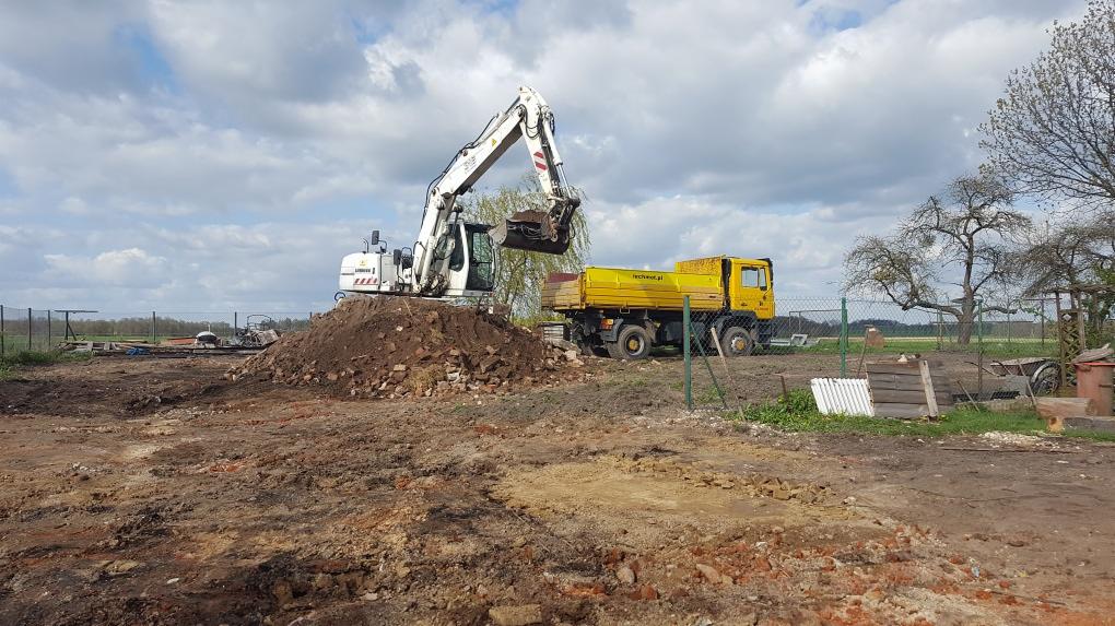 Biała koparka Liebherr nabiera gruz z pryzmy obok żółtej ciężarówki na placu budowy w słoneczny dzień.
