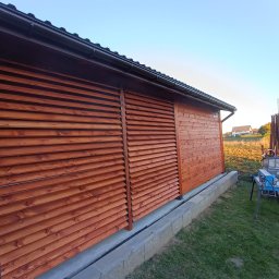 Drew Stol - Drewniana konstrukcja z lamelami i deskami w kolorze brązowym, widoczne elementy dachu, narzędzia i materiały budowlane w tle, prawdopodobnie w trakcie montażu lub tuż po nim.