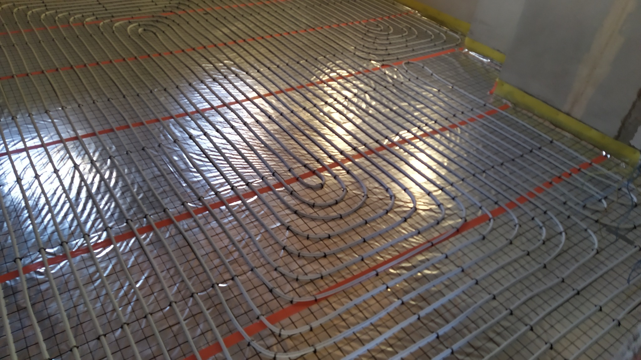 Układanie rur ogrzewania podłogowego na folii izolacyjnej z widocznymi czerwonymi paskami mocującymi