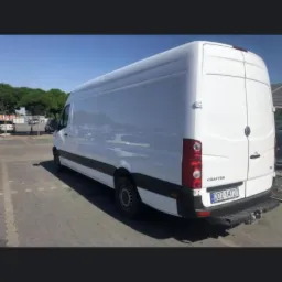 Biały bus marki Volkswagen Crafter, zaparkowany na parkingu, widoczny z tyłu pod kątem, z widoczną tablicą rejestracyjną.