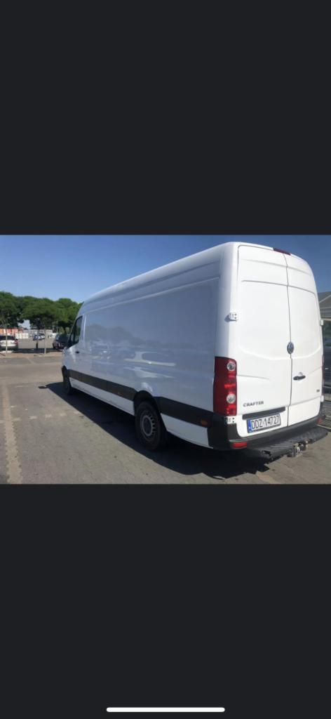 Biały bus marki Volkswagen Crafter, zaparkowany na parkingu, widoczny z tyłu pod kątem, z widoczną tablicą rejestracyjną.