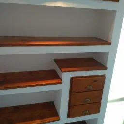 Wnęka ścienna z drewnianymi półkami i trzema szufladami z mosiężnymi uchwytami, wykończona w stylu rustykalnym.