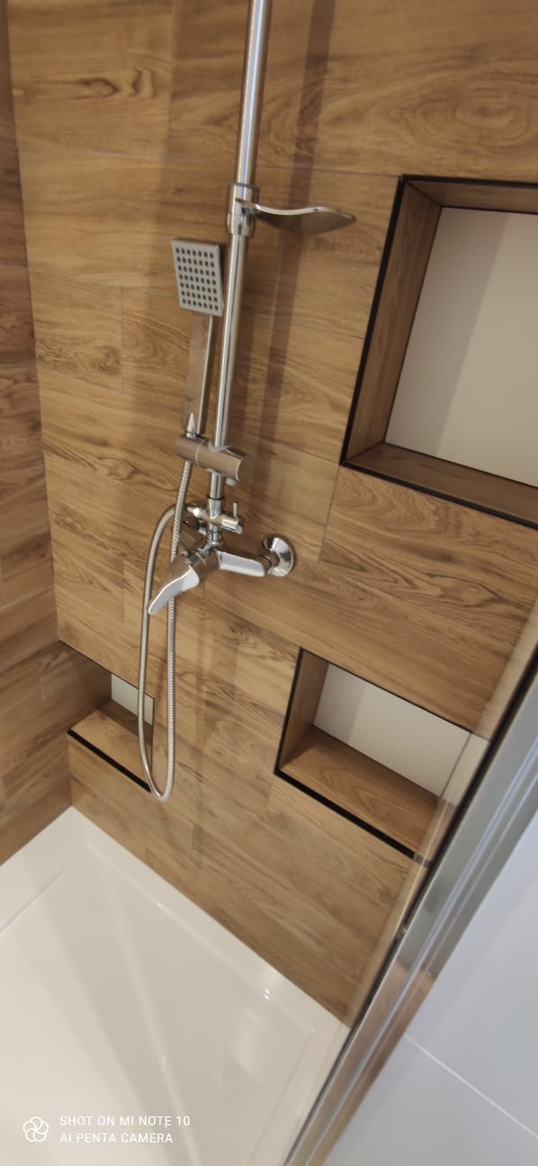 Nowoczesna kabina prysznicowa z drewnopodobnymi płytkami i wnękami na kosmetyki, chromowana armatura.