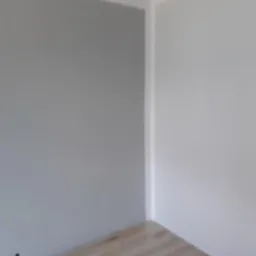 Pomieszczenie po odświeżeniu: ściana w odcieniach szarości kontrastuje z białą ścianą i listwą przypodłogową, widoczna drewniana podłoga.