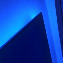 Niebieskie oświetlenie LED akcentujące krawędź ściany i dekoracyjną fakturę ściany imitującą kamień.