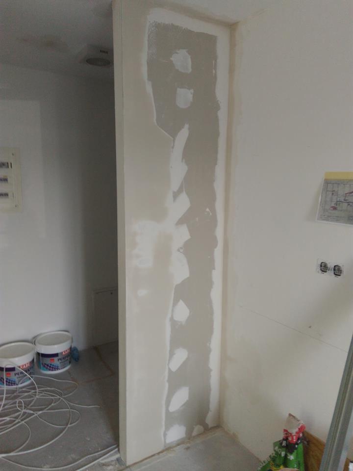 Wyrównywanie ubytku w ścianie gipsem szpachlowym, widoczne dwa wiadra szpachli na podłodze i przewody elektryczne.