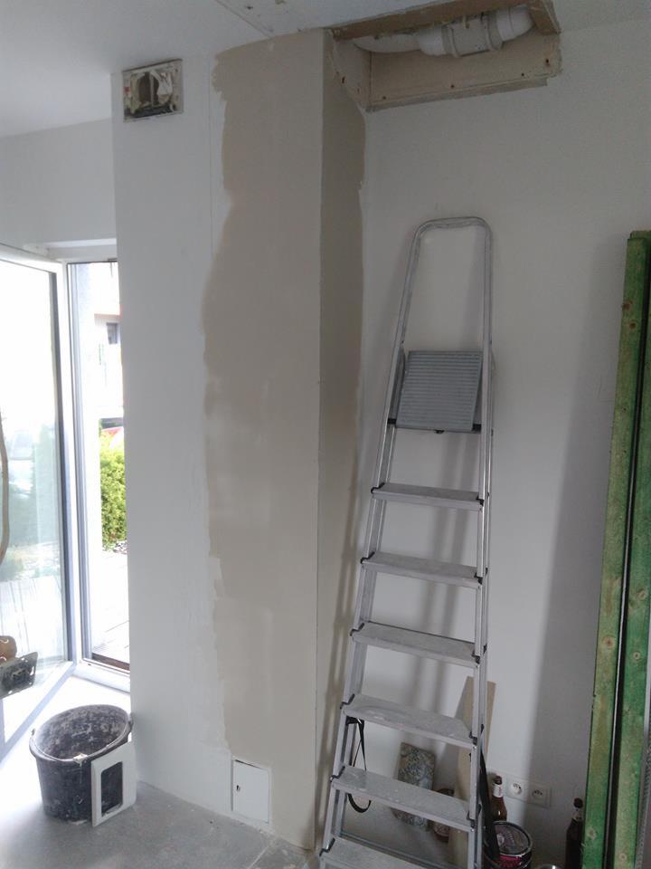 Fragment ściany po nałożeniu pierwszej warstwy gładzi, widoczna drabina aluminiowa, wiadro i butelka po piwie, instalacja sanitarna pod sufitem.