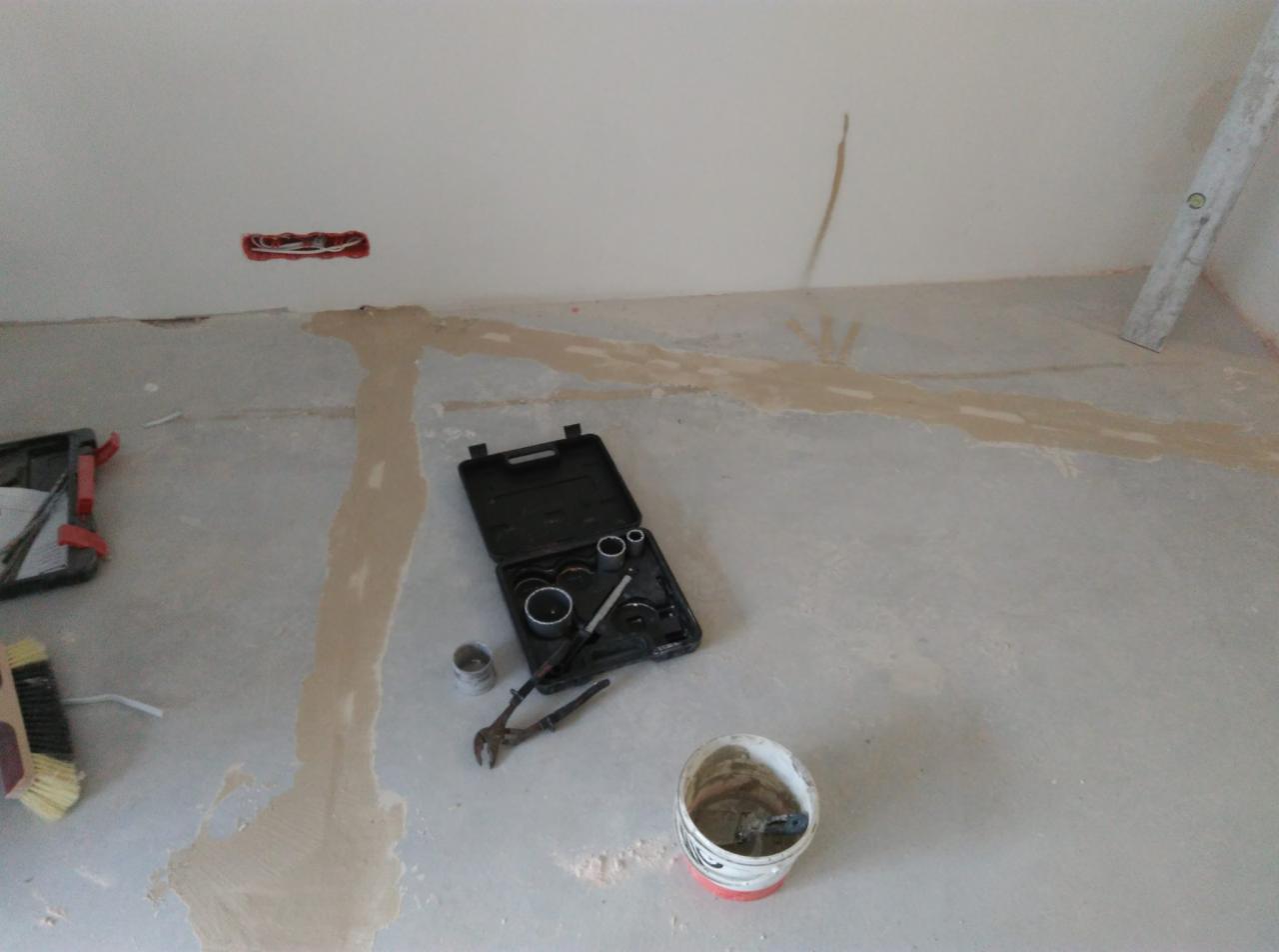 Przygotowane podłoże pod płytki z widocznymi śladami szpachlowania, skrzynka z narzędziami glazurniczymi, wiadro z zaprawą i szczotka na podłodze.