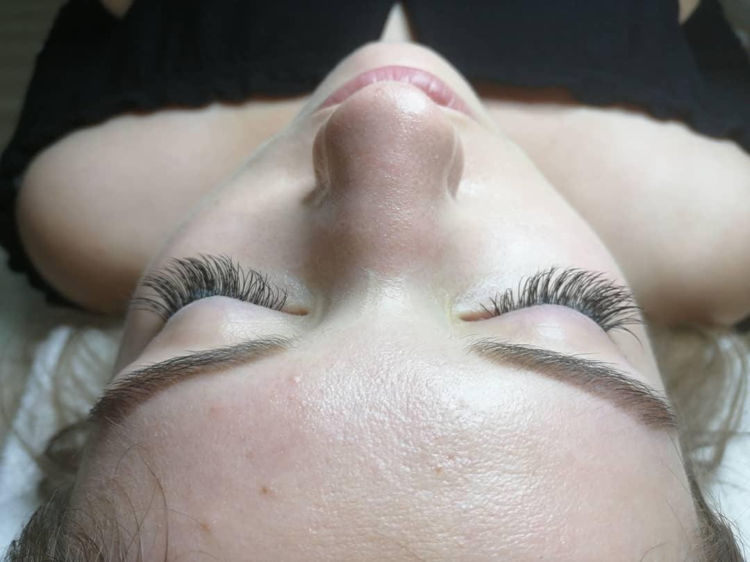 Zbliżenie na twarz kobiety z przedłużonymi rzęsami, widoczne brwi po zabiegu laminacji i delikatny makijaż ust.