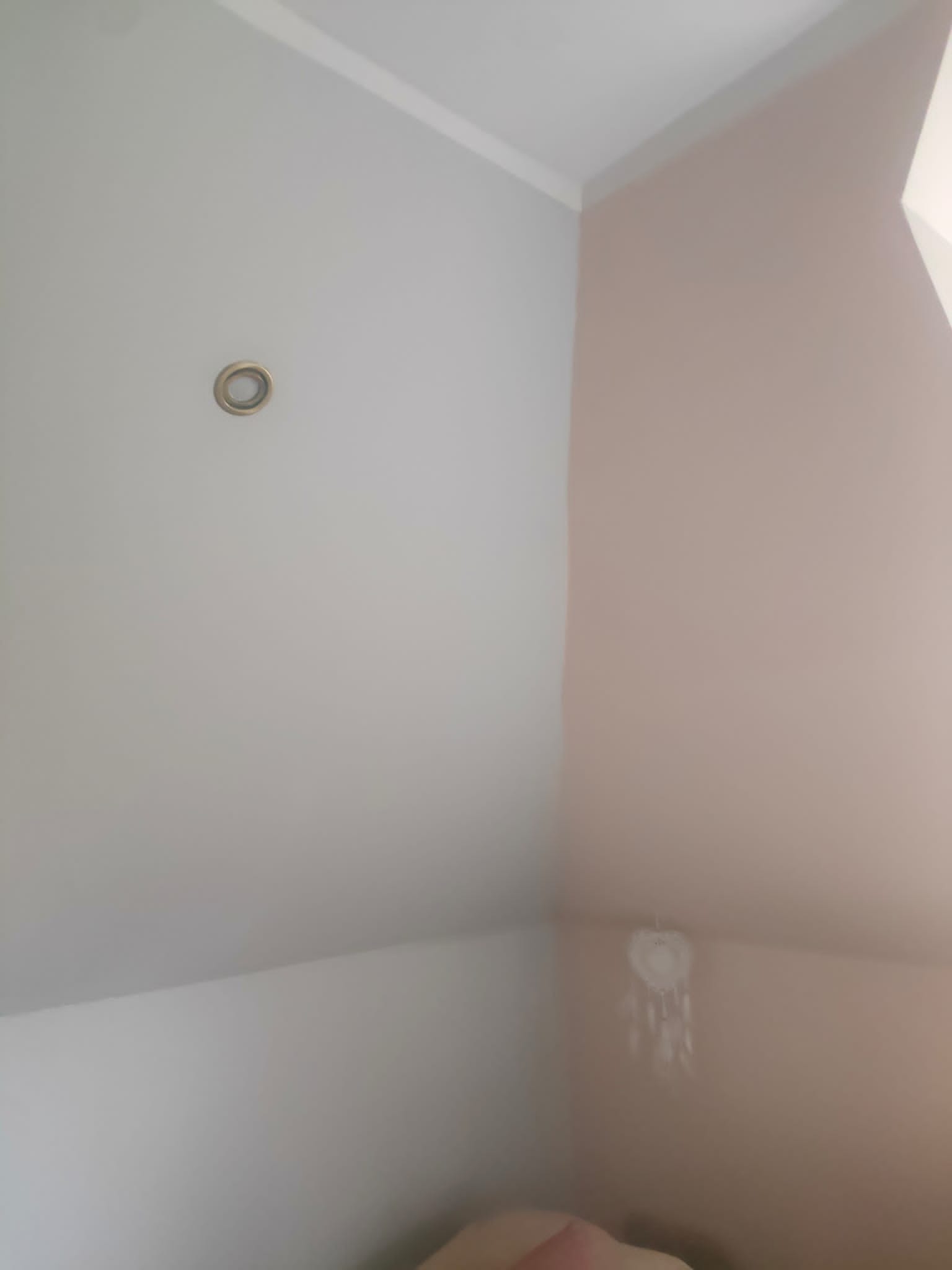 Pomalowany fragment pokoju na poddaszu w odcieniach szarości i pudrowego różu, widoczny fragment lampy sufitowej i łapacz snów.