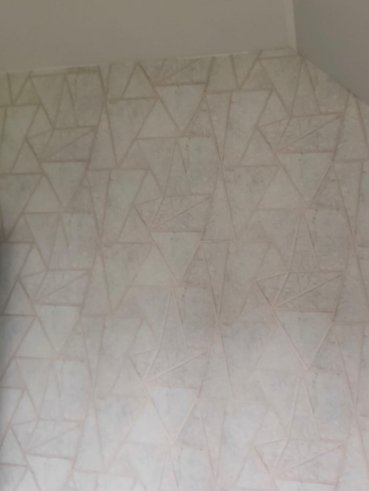 Ściana pomalowana w geometryczne wzory, jasne tło z delikatnymi, trójkątnymi liniami. Minimalistyczny design w neutralnej kolorystyce.