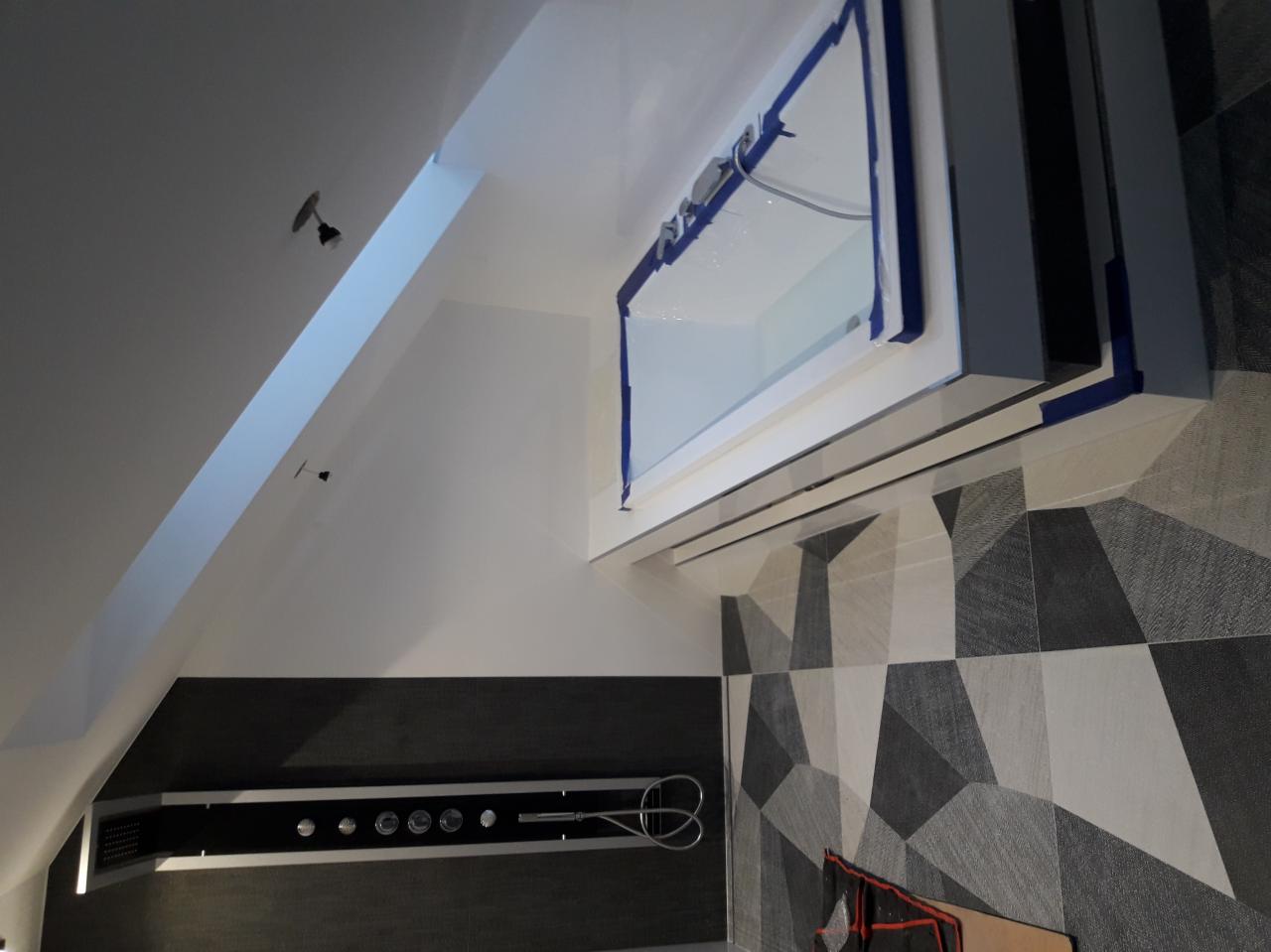 Nowoczesna łazienka w trakcie remontu: oszklona kabina prysznicowa z niebieską taśmą malarską zabezpieczającą, geometryczne płytki na ścianie, czarna ściana z chromowaną armaturą