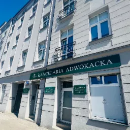 Elewacja kamienicy z szyldem 'Kancelaria Adwokacka' w słoneczny dzień, widoczne okna i balkony.