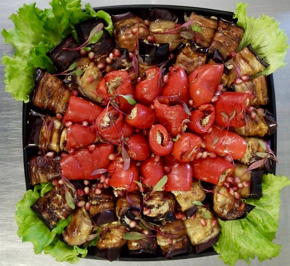 Elegancka kompozycja grillowanych rolad z bakłażana i papryki faszerowanej na czarnym talerzu, udekorowana granatem i świeżą sałatą.