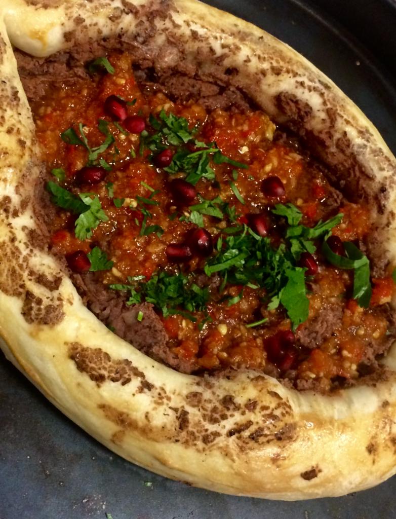 Chaczapuri Adżaruli z fasolowym farszem, pomidorową salsą, posypane granatem i świeżą kolendrą, podane na ciemnym talerzu.