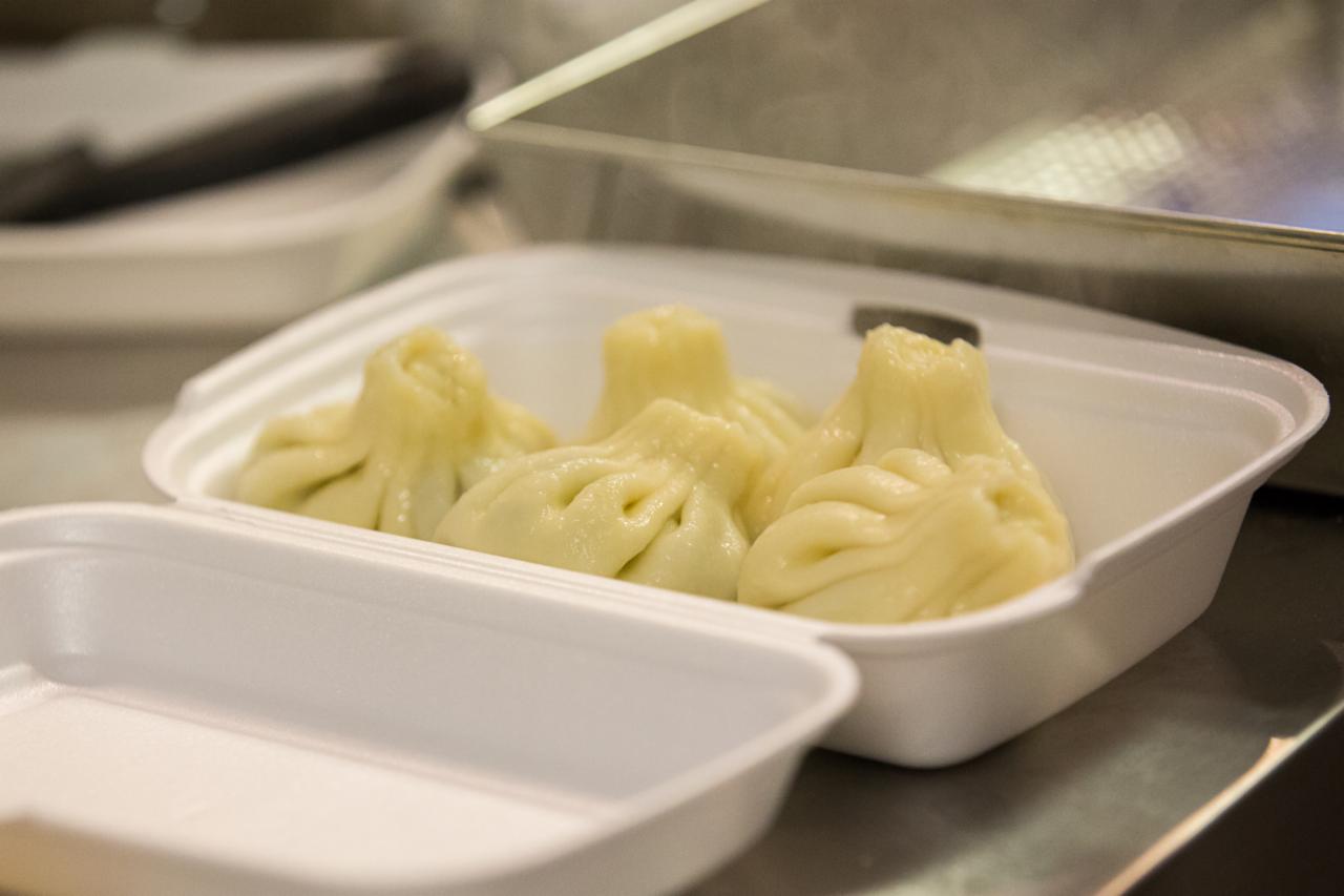 Chinkali w białym styropianowym pojemniku na wynos, widoczne fałdy ciasta i otwór na górze, gotowe do spożycia.