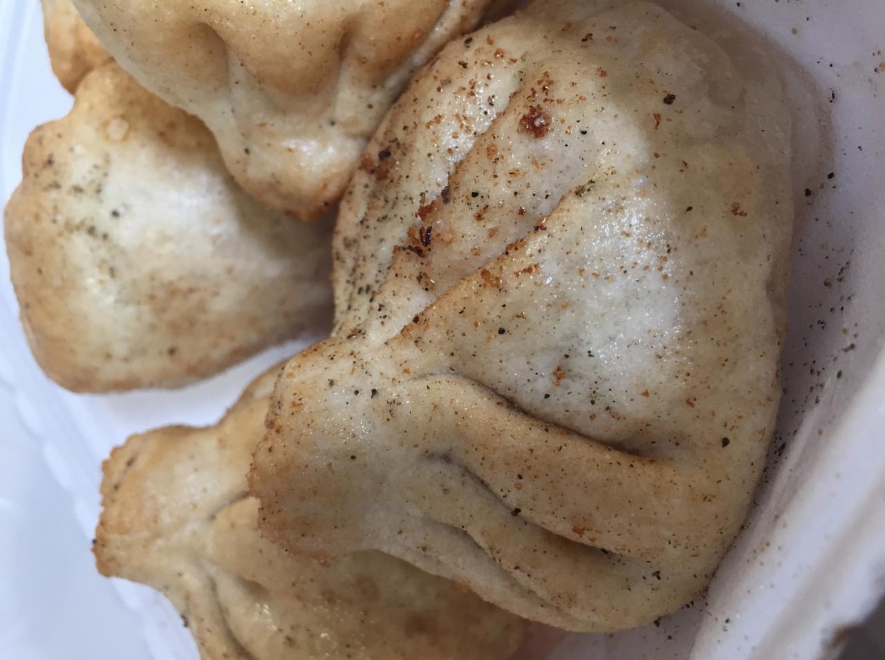 Cztery gruzińskie pierożki chinkali w białym pojemniku, posypane przyprawami, z widocznymi drobnymi plamkami i nierównościami na cieście.