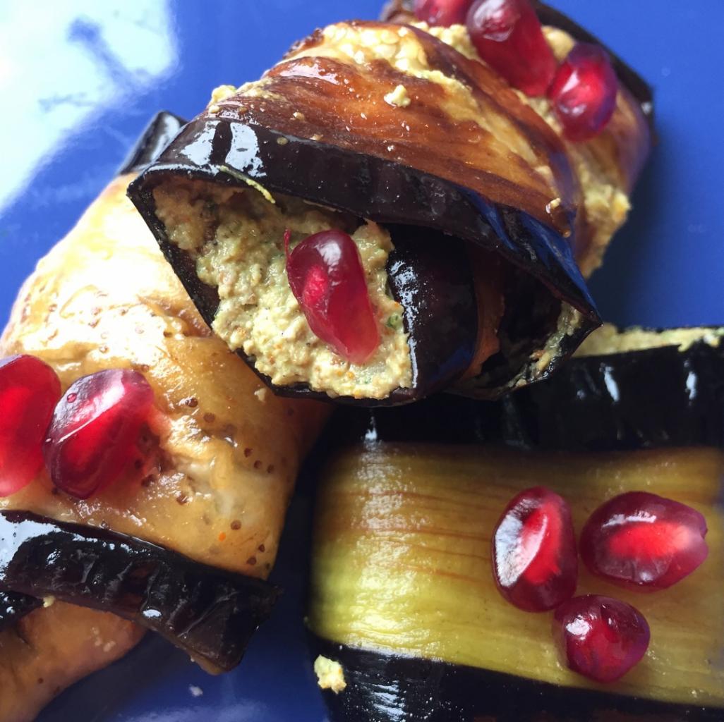 Roladki z bakłażana wypełnione pastą i udekorowane granatem na niebieskim talerzu, z widoczną teksturą bakłażana.