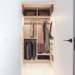 Wyskkuchnie - Otwarta, jasna garderoba wnękowa z ubraniami na wieszakach i półkach, widoczna z korytarza. Minimalistyczny design, ciepłe oświetlenie.