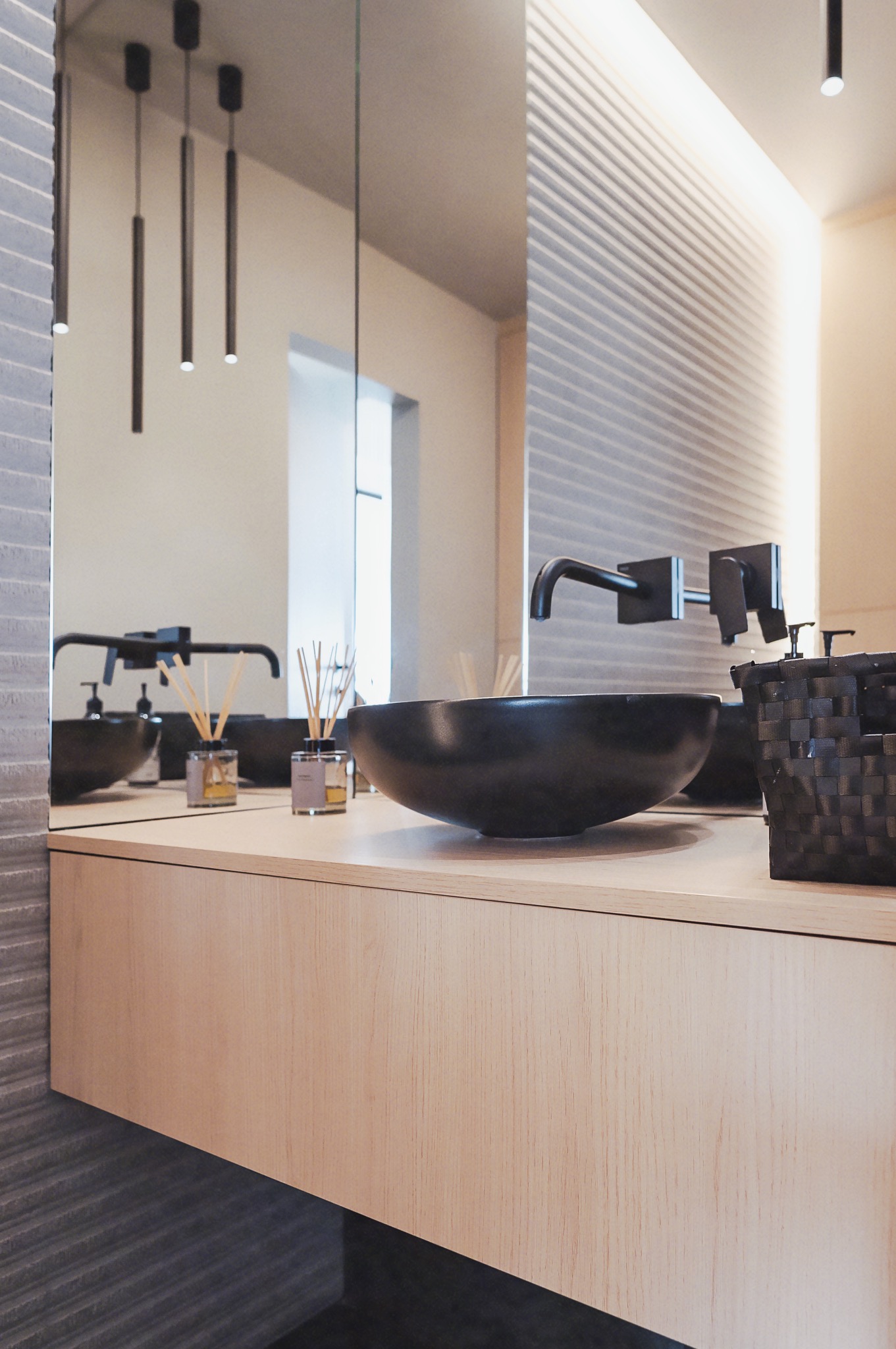 Nowoczesna szafka łazienkowa z blatem z jasnego drewna, czarną umywalką i minimalistyczną armaturą. W tle lustro i dekoracyjna ściana z podświetleniem LED.