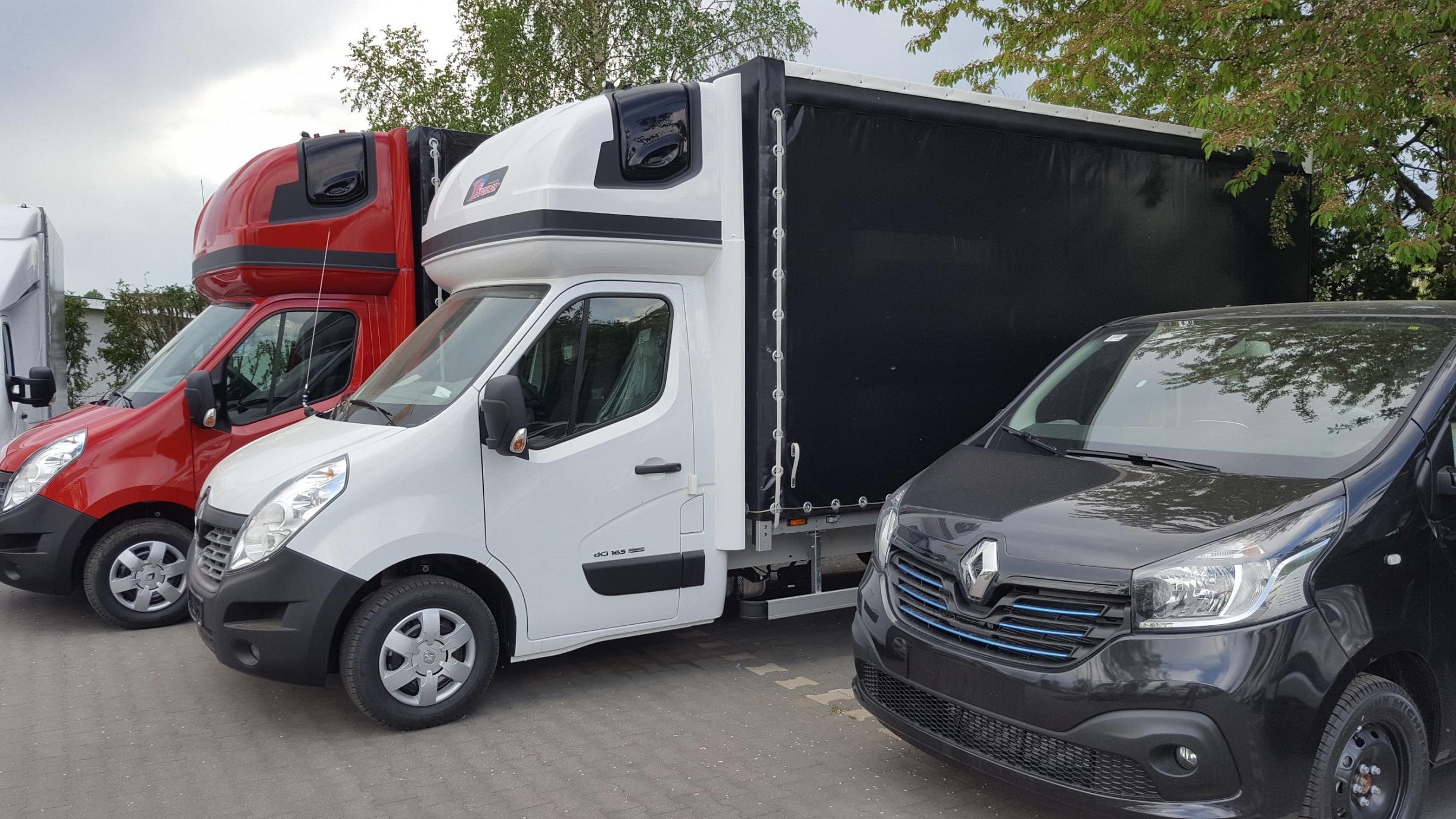 Rząd zaparkowanych samochodów dostawczych Renault Master z zabudową kontenerową, widok z boku, z czarną plandeką na jednym z nich.
