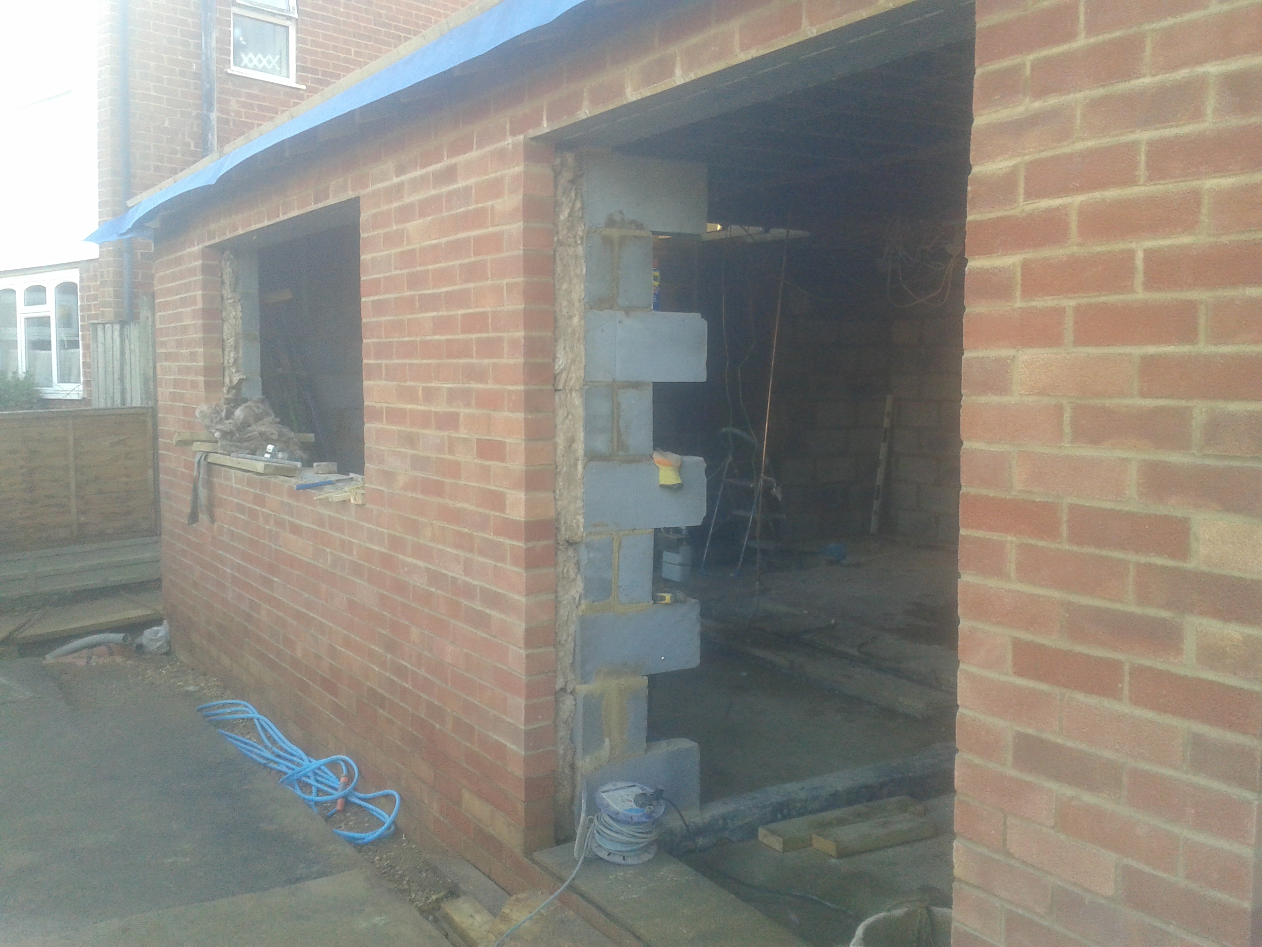 Murowana konstrukcja w trakcie budowy, widoczne cegły, pustaki i przewody elektryczne wewnątrz budynku.