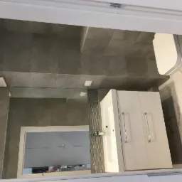 Wykończona łazienka z szarymi płytkami na ścianach i podłodze, białą szafką z umywalką i toaletą, marmurową ścianą oraz lustrem z mozaiką.