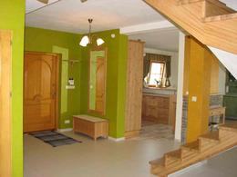 Jasne wnętrze domu po remoncie: zielone ściany, drewniane drzwi wejściowe, lustro w drewnianej ramie, drewniana ławka przy ścianie, widoczne schody z drewnianymi stopniami, fragment kuchni w tle...