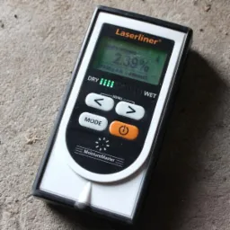 Miernik wilgotności Laserliner MoistureMaster wskazujący wartość 2.39% na wyświetlaczu, leżący na szarej powierzchni.