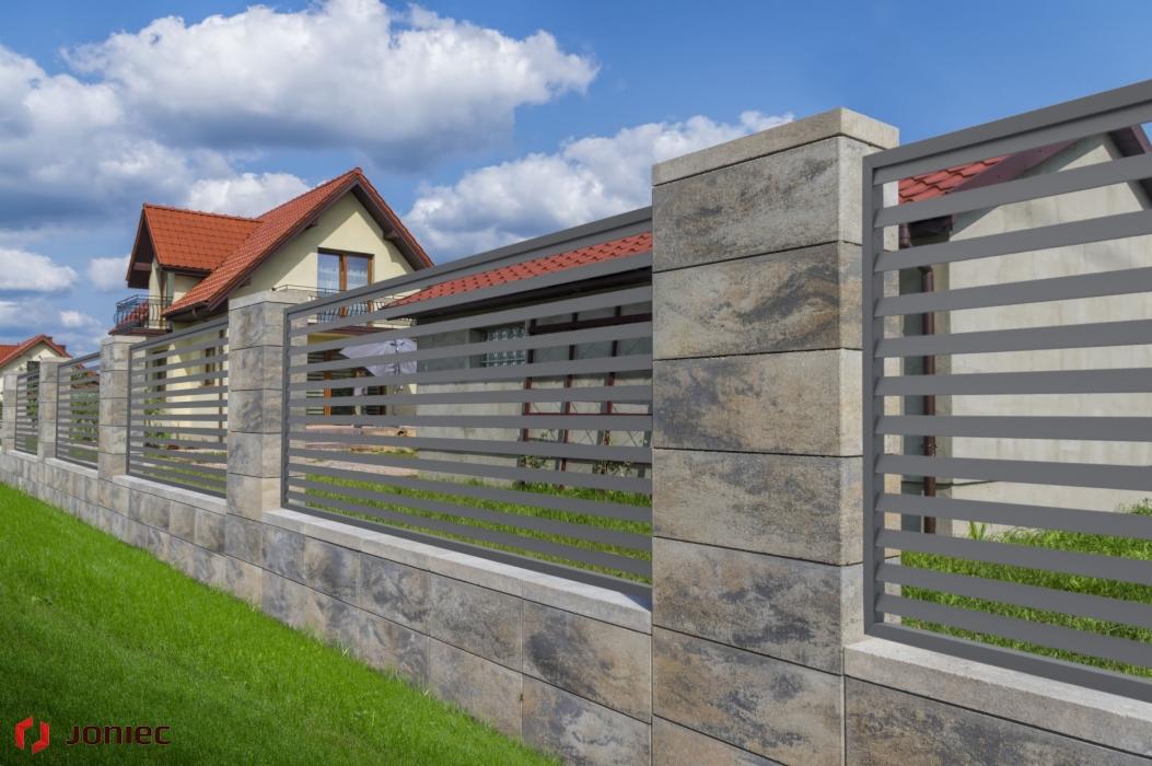 Nowoczesne ogrodzenie z szarych paneli poziomych i słupków z betonu architektonicznego na tle zielonego trawnika i domu z czerwoną dachówką.