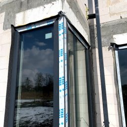 MAST - Śląskie Okna - Narożne okno z profili Veka w surowym stanie, widoczne detale montażu i pianka izolacyjna. W szybie odbija się zimowy krajobraz.