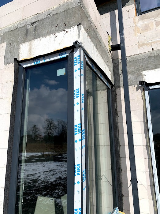 Narożne okno z profili Veka w surowym stanie, widoczne detale montażu i pianka izolacyjna. W szybie odbija się zimowy krajobraz.