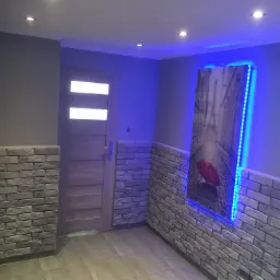 Wykończone wnętrze: szara ściana z dekoracyjną cegłą, drewniane drzwi z przeszkleniami, obraz z podświetleniem LED przedstawiający ulicę Paryża z czerwoną parasolką.