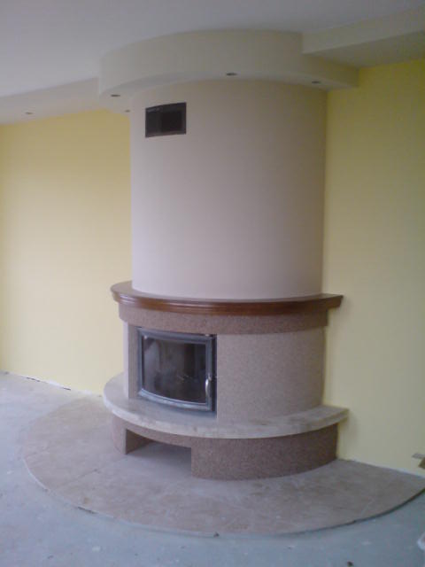 Otynkowany kominek z brązowym blatem i marmurową podstawą, w jasnym pomieszczeniu z żółtą ścianą.