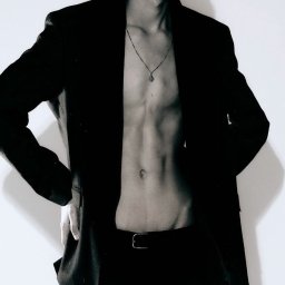 Fotografia niekonwencjonalna Ilona Bałon - Czarno-biały portret mężczyzny w marynarce, bez koszuli, z łańcuszkiem, pozującego na jasnym tle. Minimalistyczny styl, ostre światło.