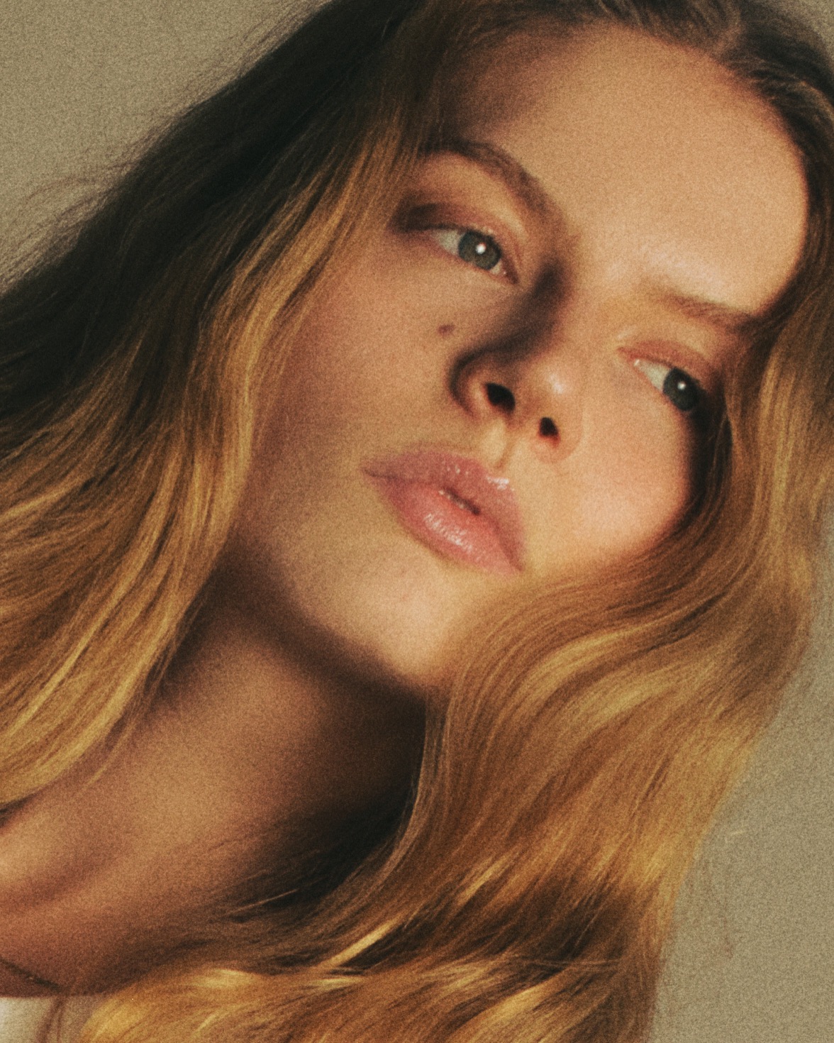Subtelny portret młodej kobiety z długimi, falowanymi włosami w ciepłej tonacji. Ujęcie z bliska, skupione na twarzy, z delikatnym cieniem podkreślającym rysy.
