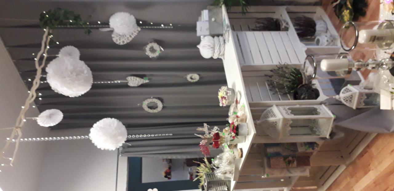 Dekoracje wiszące (białe pompony, girlandy) i stojące (kwiaty w wazonach, lampiony) tworzące aranżację eventową, widoczne z perspektywy lekko od dołu.