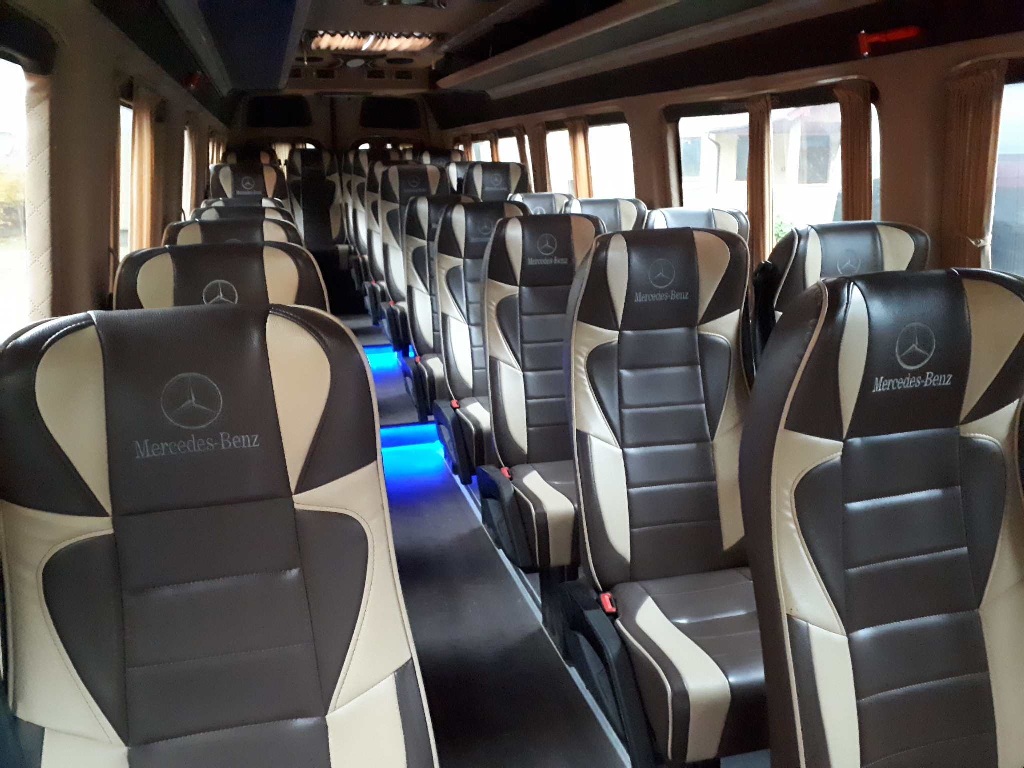 Wnętrze autobusu z brązowo-beżowymi skórzanymi fotelami z logo Mercedes-Benz, oświetlenie podłogowe LED w kolorze niebieskim.
