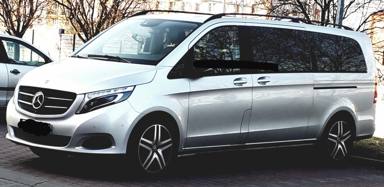 Srebrny Mercedes-Benz V-klasy z relingami dachowymi, zaparkowany na zewnątrz w pochmurny dzień.