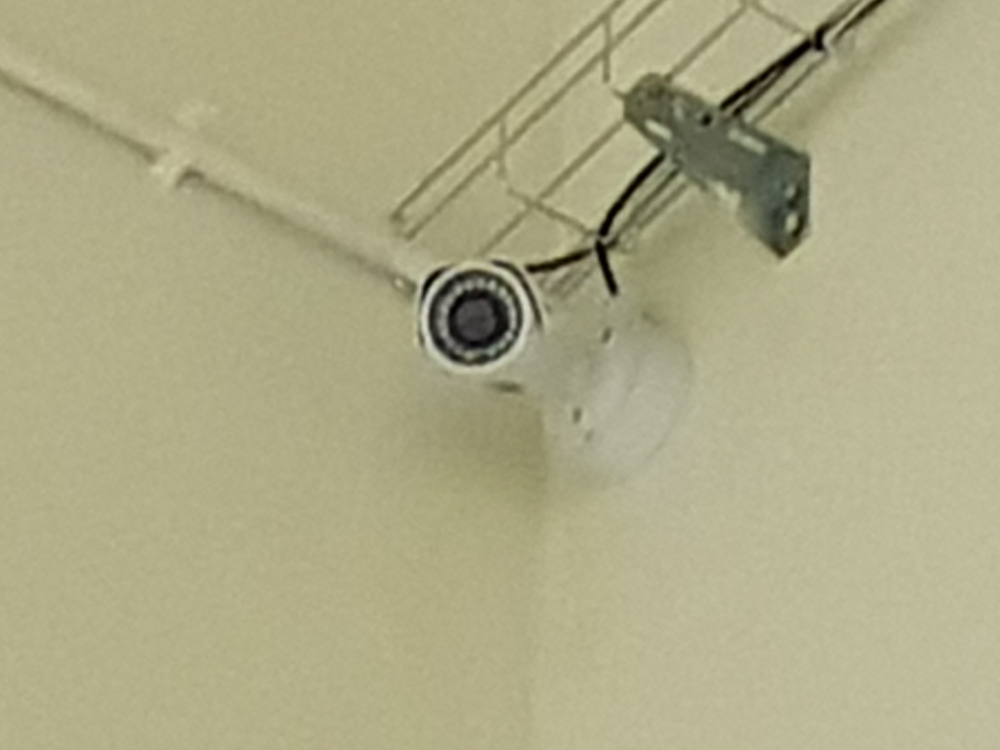 Kamera monitoringu zamontowana pod sufitem, widoczne okablowanie w metalowej listwie.