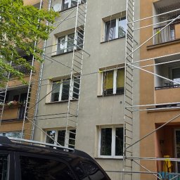 DEKARBUD ADAM MADZIAR - Praca na rusztowaniu przy elewacji budynku w Mińsku Mazowieckim. Dwóch mężczyzn na górze, widoczne okna i fragment zaparkowanego samochodu.